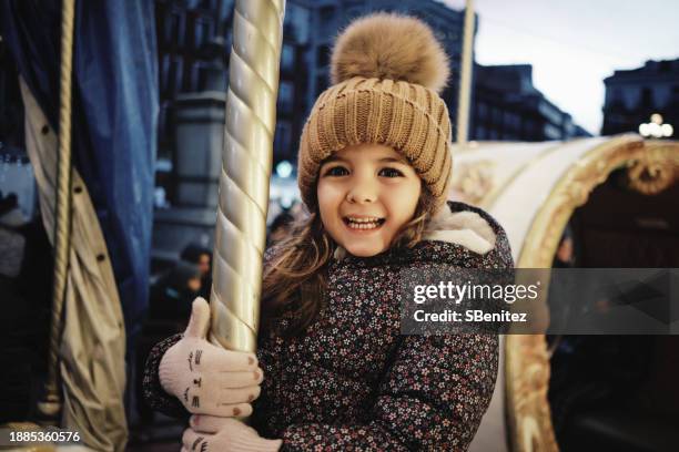 girl riding a carousel at a christmas market - bonnet à pompon photos et images de collection