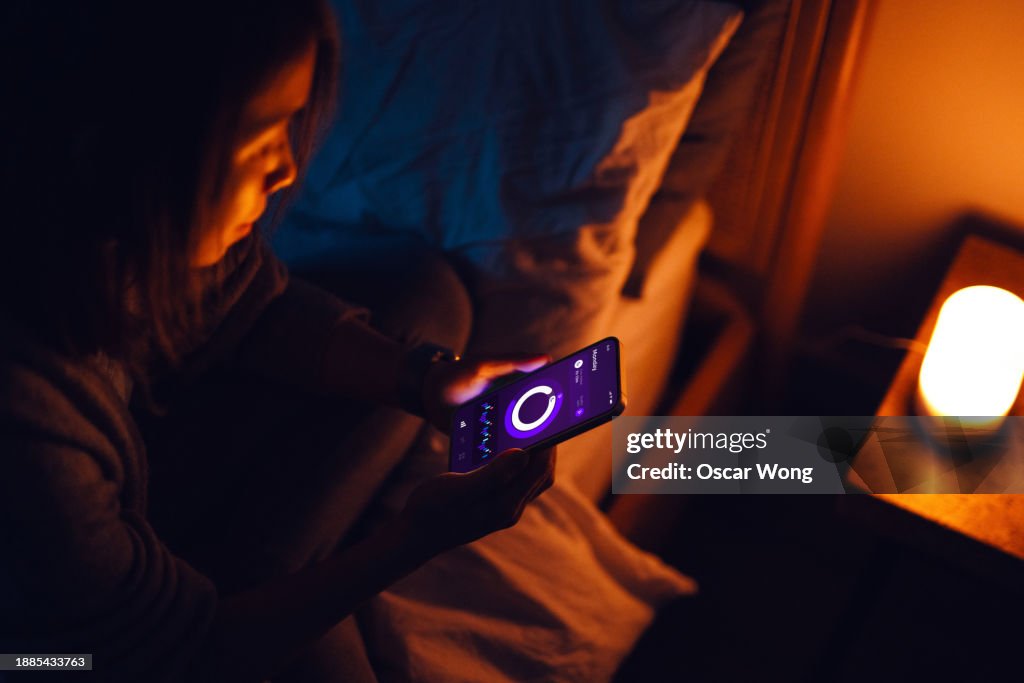 Young Asian woman using sleep tracker app on smartphone to monitor her sleep cycle