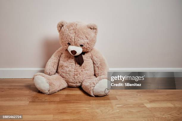 the big sad teddy bear is sitting on a wooden floor crestfallen - peluche foto e immagini stock
