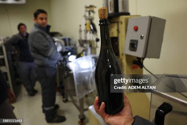 An employee shows a sparkling wine bottle after the disgorging process aimed at improving the aromatic personality of sparkling wine at Vinkara...