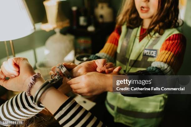 a little girl, dressed as a police officer, handcuffs an adult with plastic handcuffs - blame game stock pictures, royalty-free photos & images