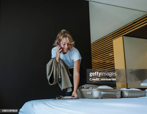 portrait of a beautiful blonde woman packing a suitcase while having a phone call - business class imagens e fotografias de stock