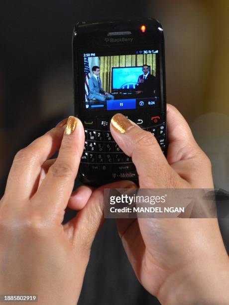 An attendee takes a photo with her cell phone as US President Barack Obama speaks during a "Twitter Town Hall" July 6, 2011 in the East Room of the...