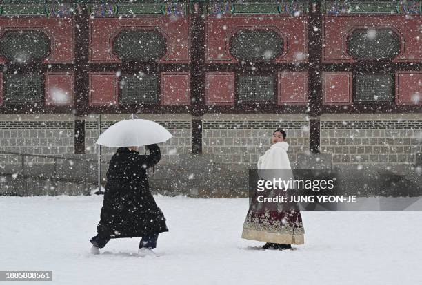 Visitors wearing traditional hanbok dress pose for photos in the snow at Gyeongbokgung palace in central Seoul on December 30, 2023.