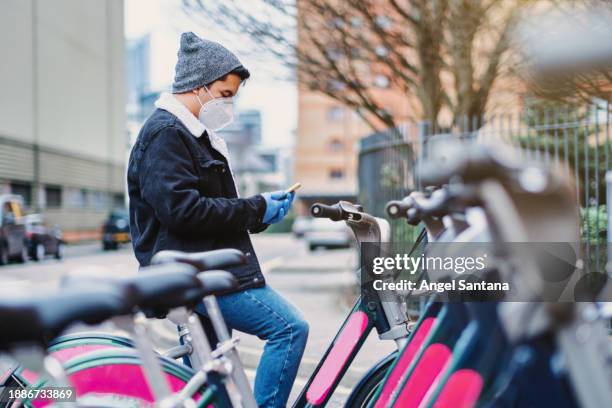 young guy in mask using smartphone near rental bikes - commuter man europe bike stock pictures, royalty-free photos & images