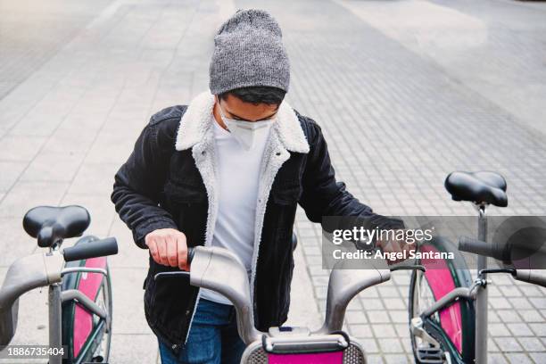 young male in mask renting bike on city street - coronavirus ward stock pictures, royalty-free photos & images