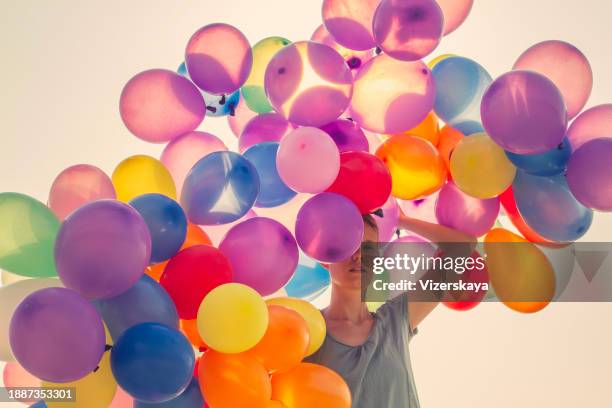 young woman walking with many balloons in sunset at the ocean beach - leicht stock-fotos und bilder