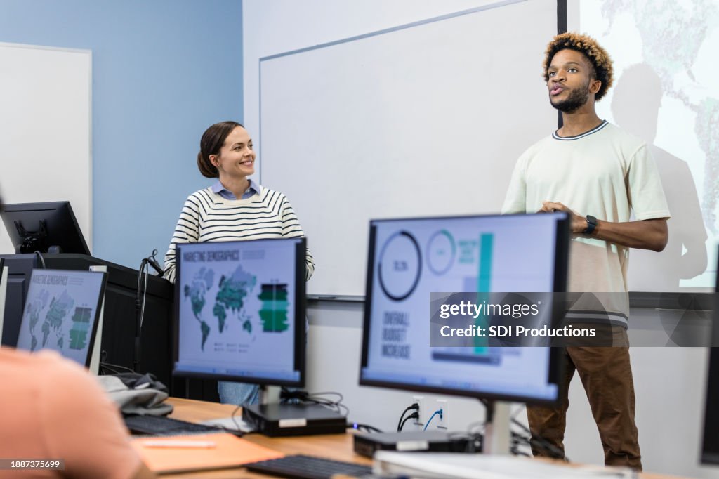 Female teacher smiles as male student presents project