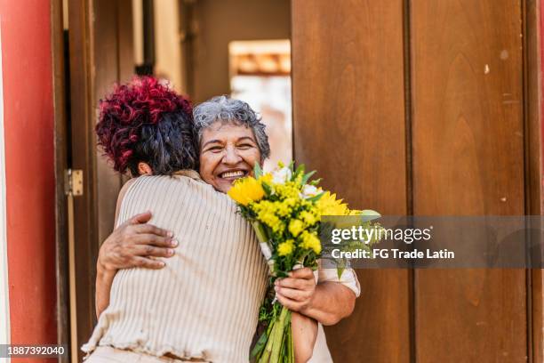 grandmother embracing her granddaughter after receiving a bouquet of flowers at home - visit grandmother stock pictures, royalty-free photos & images