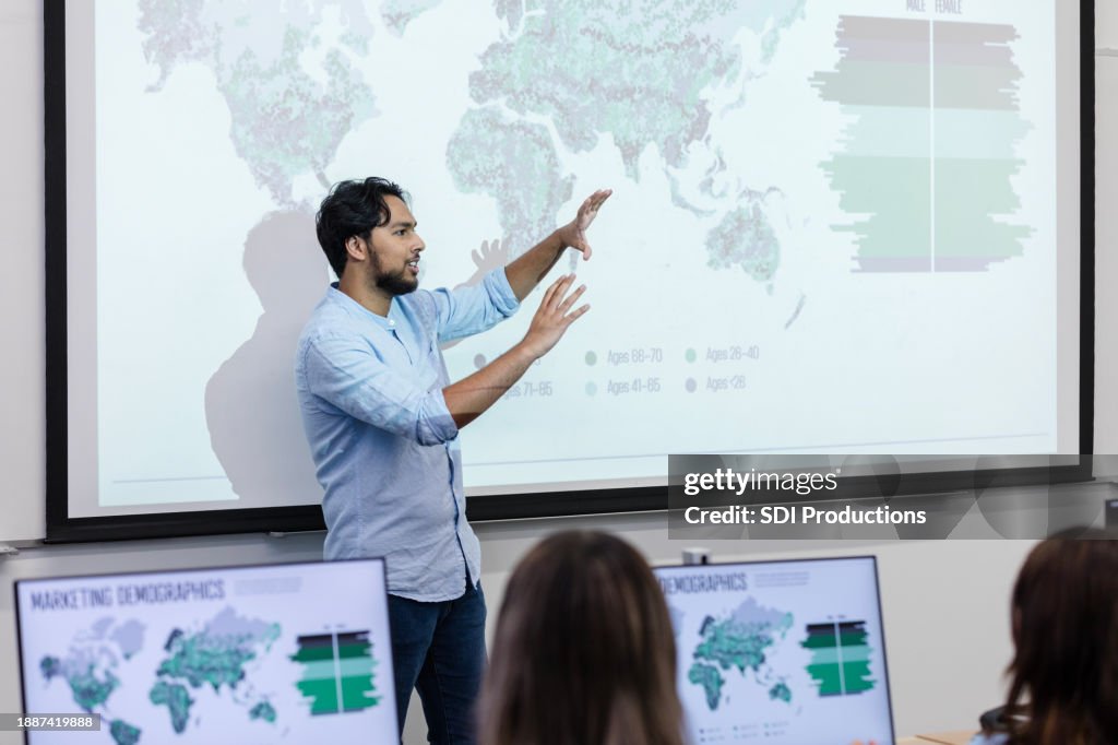 Mid adult male supervisor stands at the front of the conference room to talk