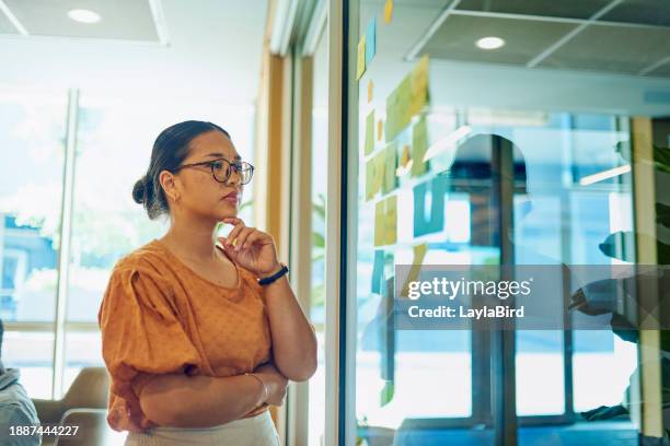 mujer de negocios pensativa que mira notas adhesivas en la pared de vidrio en la oficina. - female execution photos fotografías e imágenes de stock