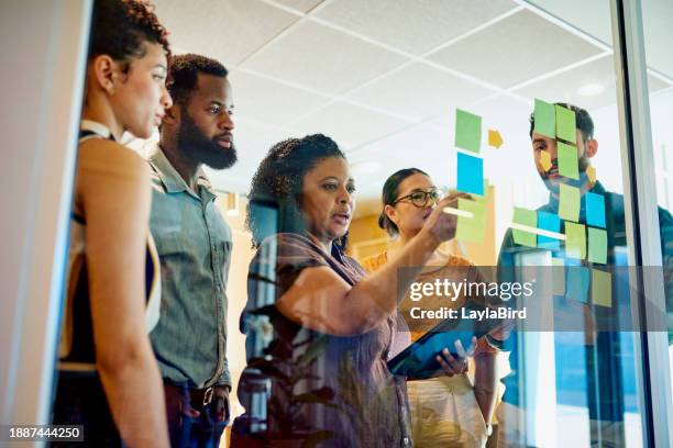 diverse professionals brainstorming on a glass wall with sticky notes - private equity stock pictures, royalty-free photos & images