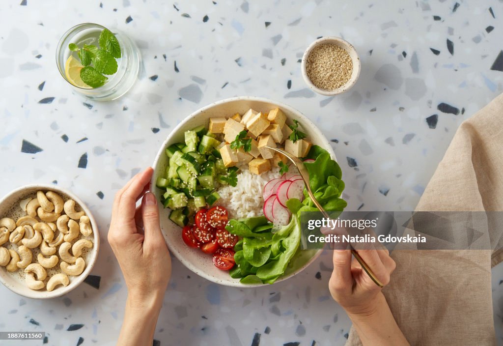 Faceless female eating vegan vegetarian salad buddha bowl - rice, tofu, cherry tomato, cucumber, radish, lettuce