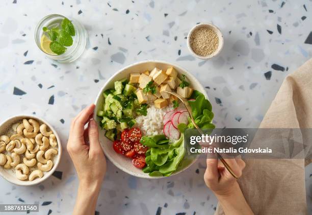 faceless female eating vegan vegetarian salad buddha bowl - rice, tofu, cherry tomato, cucumber, radish, lettuce - cashew pieces stock pictures, royalty-free photos & images