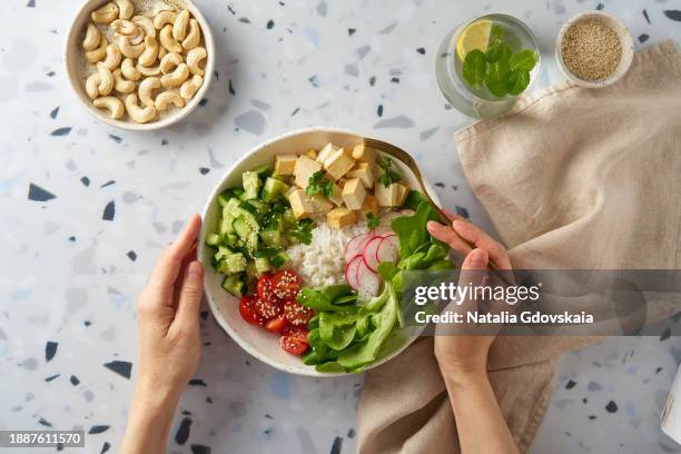 faceless female eating vegan vegetarian salad buddha bowl - rice, tofu, cherry tomato, cucumber, radish, lettuce - cashew pieces stock pictures, royalty-free photos & images