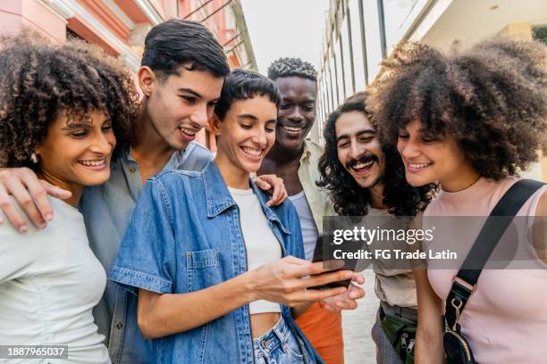 young woman showing something on mobile phone to her friends outdoors - cuban ethnicity stock pictures, royalty-free photos & images