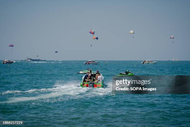 Boat carrying tourists for water activities is seen on the sea, with in the background tourists playing parasailing at Pattaya Beach. Pattaya Beach...