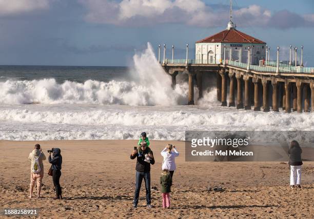 Manhattan Beach resident Martin Leikarts center, takes a selfie with his son Frederick on his shoulders as another large wave crashes against the...