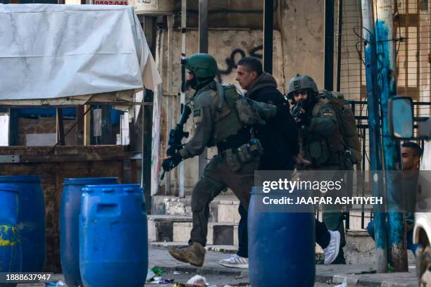 Israeli soldiers arrest a man during a raid in the Askar refugee camp, east of the occupied West Bank city of Nablus on December 31, 2023.