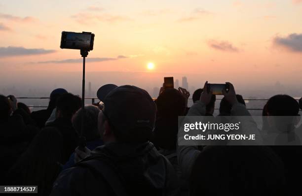 People take pictures as they observe the last sunset of the year on a viewing deck at Namsan tower in Seoul on December 31, 2023.