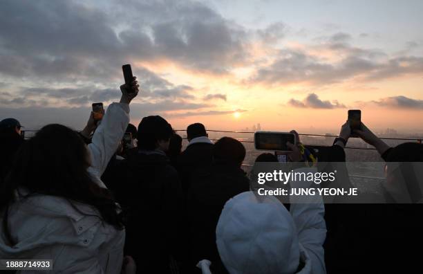 People take pictures as they observe the last sunset of the year on a viewing deck at Namsan tower in Seoul on December 31, 2023.