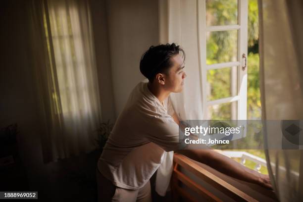 uomo che guarda attraverso la finestra al mattino - aprire foto e immagini stock