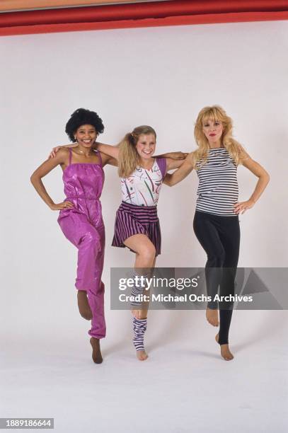 Three women modelling exercise wear, one wearing a fuchsia-coloured leisure suit, another wearing a black-and-purple striped skirt with a t-shirt...