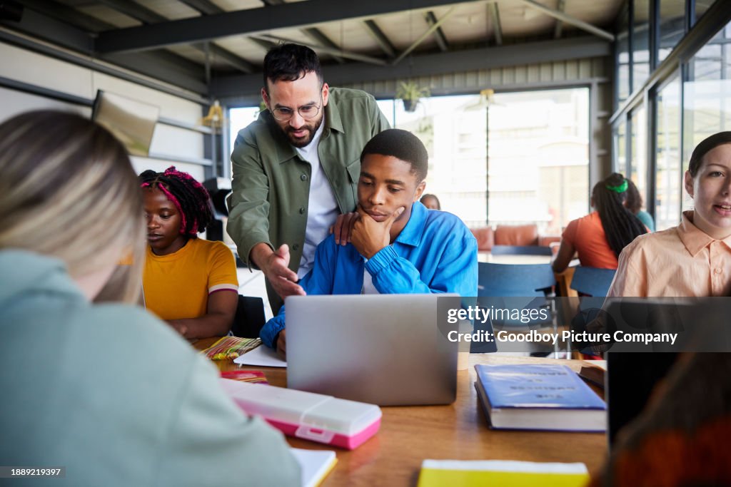 Teacher helping a student working on a laptop in a college cafeteria