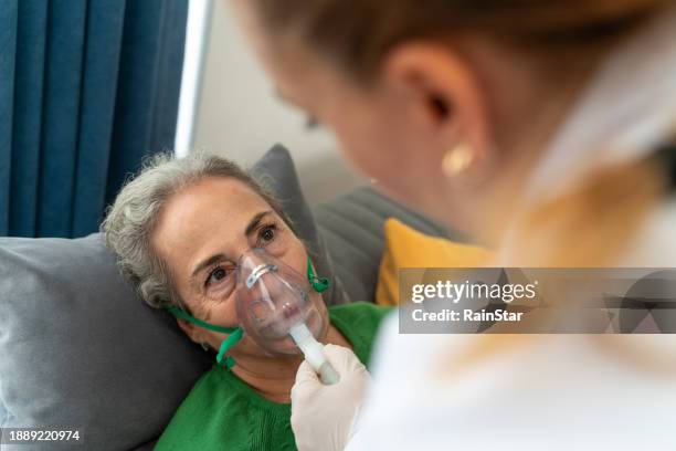 médico ayudando a una mujer mayor a poner una mascarilla facial inhaladora de nebulizador en casa - oxígeno fenómeno natural fotografías e imágenes de stock