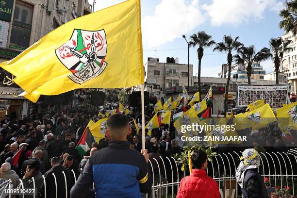 Palestinians lift flags during a rally marking the 59th anniversary of the Fatah movement foundation in Ramallah in the occupied West Bank on...