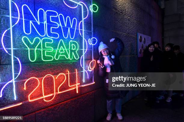 Woman poses for a photo in front of a 2024 luminous sign before a countdown event to celebrate the New Year in central Seoul on December 31, 2023.