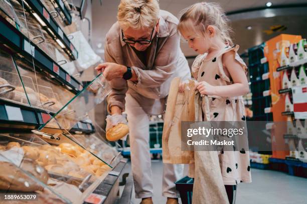 senior woman buying bread with granddaughter holding bags at grocery store - supermarket bread stock pictures, royalty-free photos & images