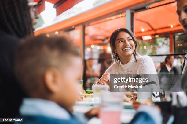smiling woman looking away while having food with family at restaurant - indian family restaurant stock pictures, royalty-free photos & images