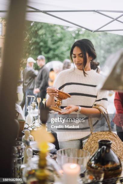 young woman buying antique standing near stall while doing shopping at flea market - rommelmarkt stockfoto's en -beelden