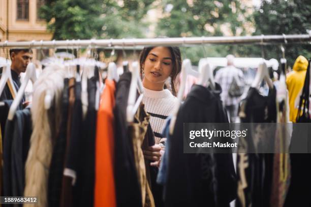young woman selecting dress hanging on clothes rack at flea market - feira da ladra mercado imagens e fotografias de stock