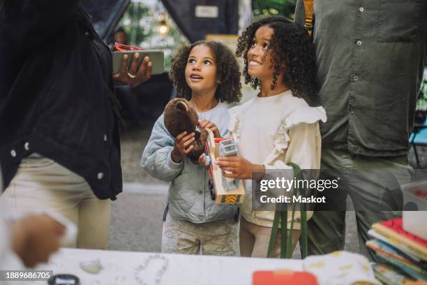 smiling female siblings looking up while holding toys at flea market - animal representation stock pictures, royalty-free photos & images