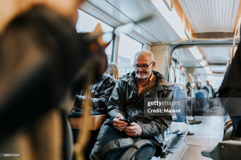 Elderly man using smart phone and sitting in bus while traveling to work