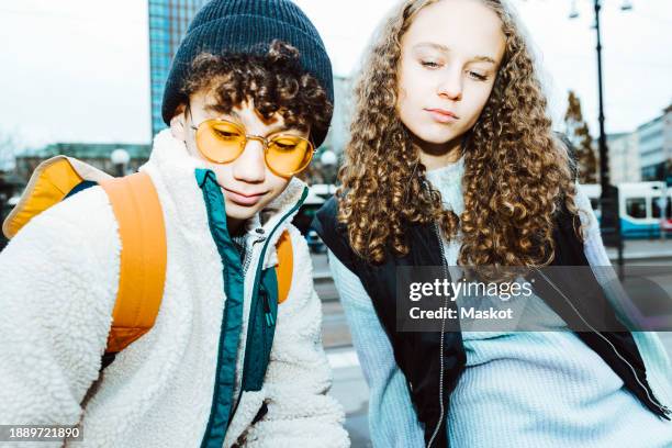 multiracial male and female friends looking down while sitting on footpath - alpha female stock pictures, royalty-free photos & images