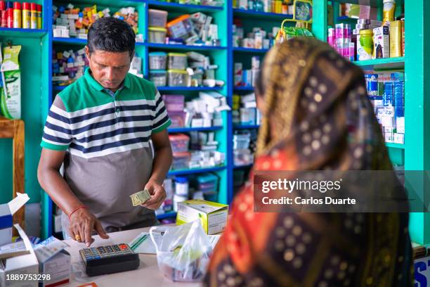 an indian pharmacist in an indian pharmacy attends to a customer sari woman who needs a medicine and caculate with the calculator the price of the drug - india lab stockfoto's en -beelden