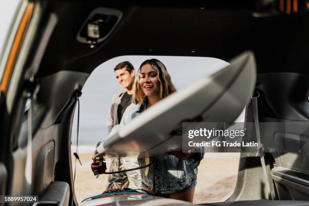 young woman picking the surfboard on car trunk at beach - surfing stock pictures, royalty-free photos & images