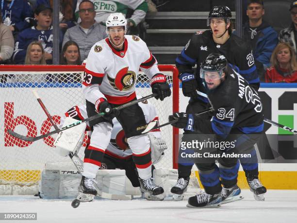 Travis Hamonic of the Ottawa Senators keeps an eye on a puck next to Auston Matthews and Matthew Knies of the Toronto Maple Leafs during the first...