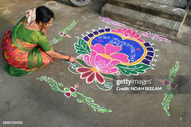 Woman applies coloured powder to a "rangoli" design to usher in the new year in front of a home in Hyderabad on January 1, 2024.