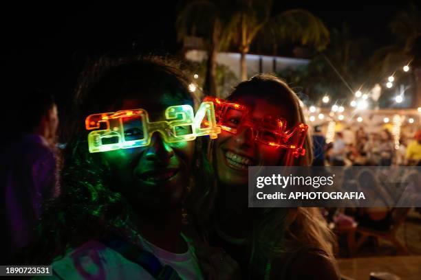 Couple smiles with glasses of lights with the year 2024 during the New Year's Eve celebration in El Tunco beach on January 01, 2024 in La Libertad,...