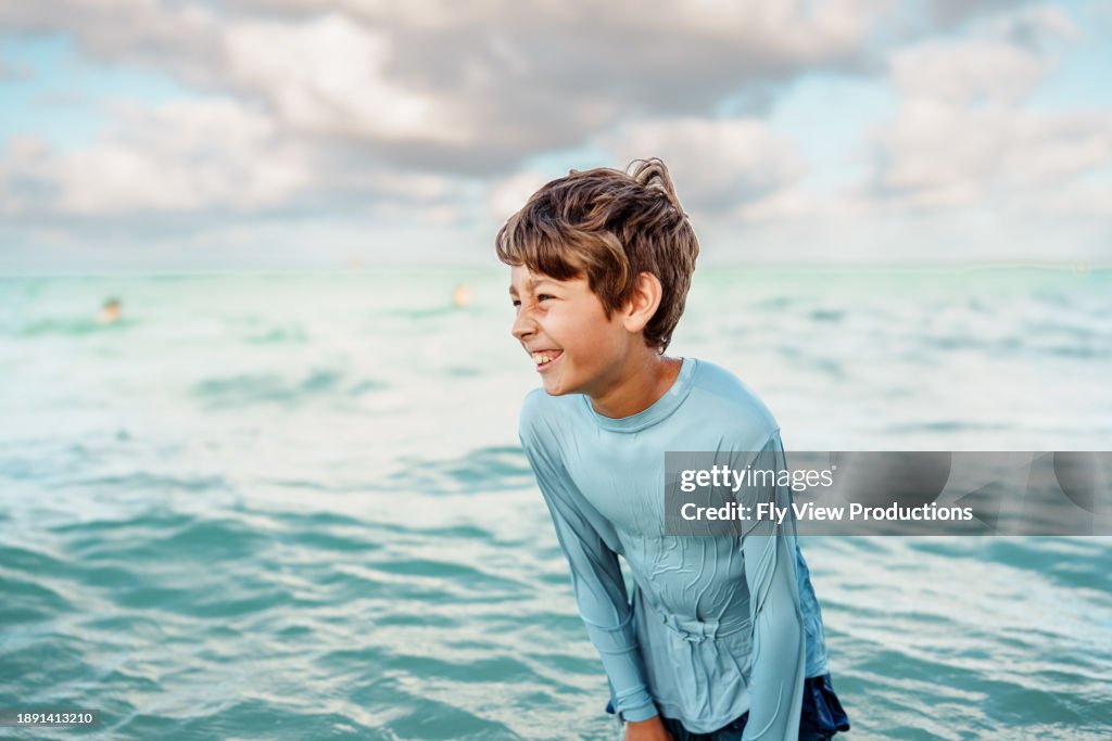 Young boy laughs while standing in the ocean