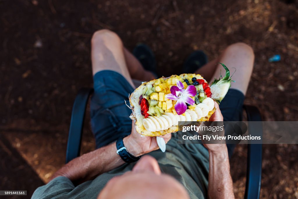 年配の男性は、外でアサイーボウルを膝で保持しています