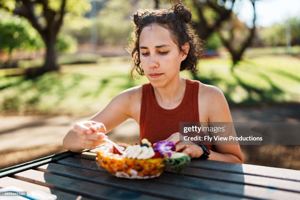 Woman eats açaí bowl on outdoor picnic table