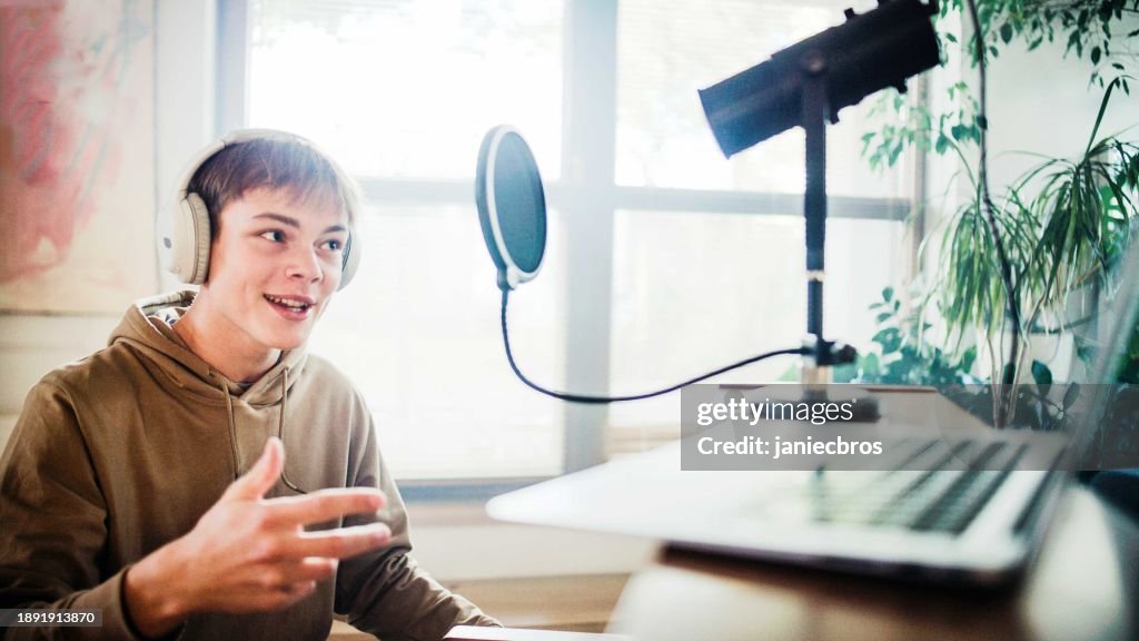 Male student wearing headphones practicing singing lessons and playing rap background music on the laptop computer