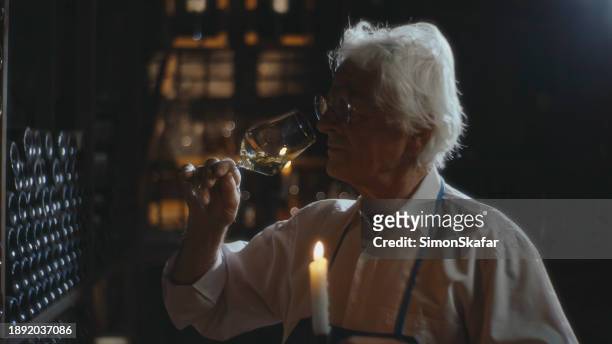 senior wine expert holding a burning candle and smelling wine in glass at his cellar - wine rack stock pictures, royalty-free photos & images