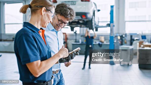 manager und mechaniker koordinieren sich mit einem mobiltelefon in der autowerkstatt - autowerkstatt stock-fotos und bilder