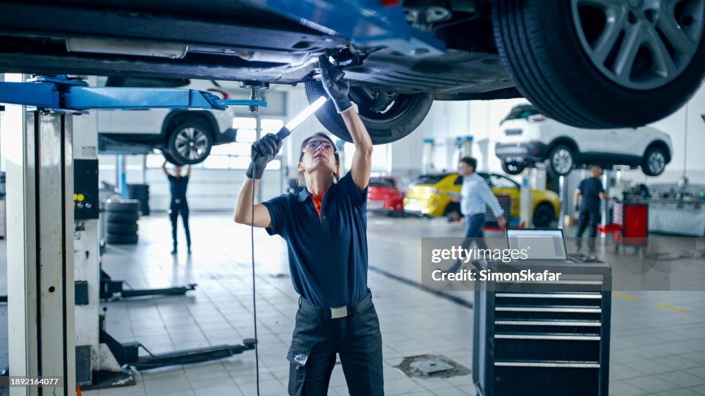 Weibliche Mechanikerin mit Licht, das unter dem Auto in der Autowerkstatt arbeitet